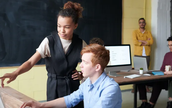 Lady pointing at monitor of seated man
