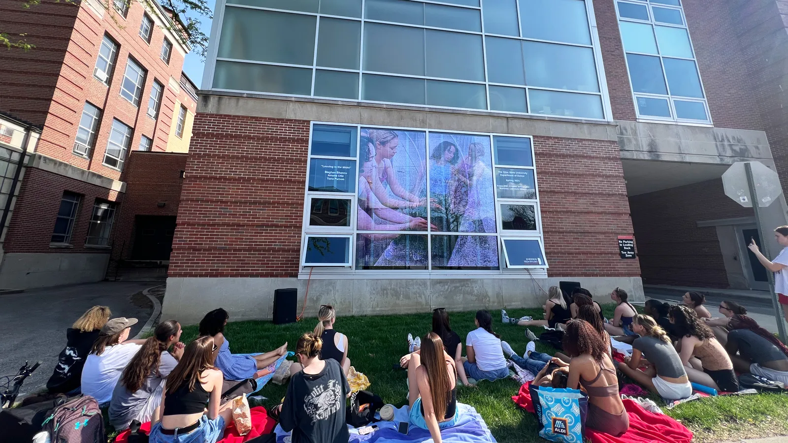 Students sitting on the lawn in front of the LED display